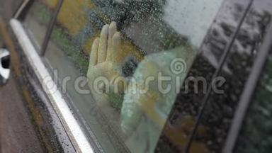 那个女孩`把手掌放在汽车的湿玻璃上